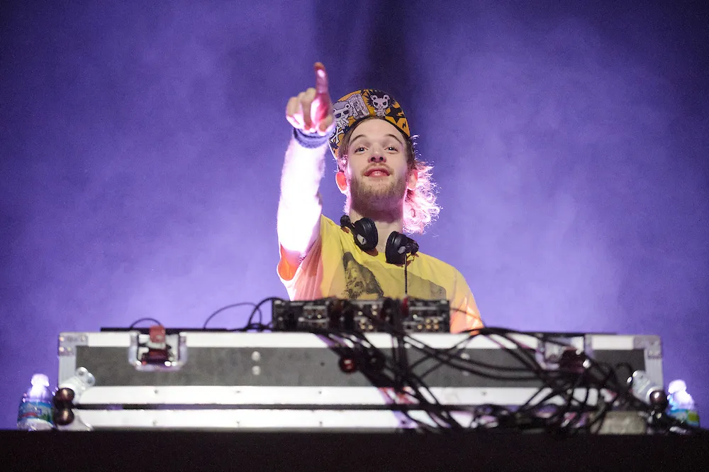 Rusko performing live on stage with a large LED screen behind him